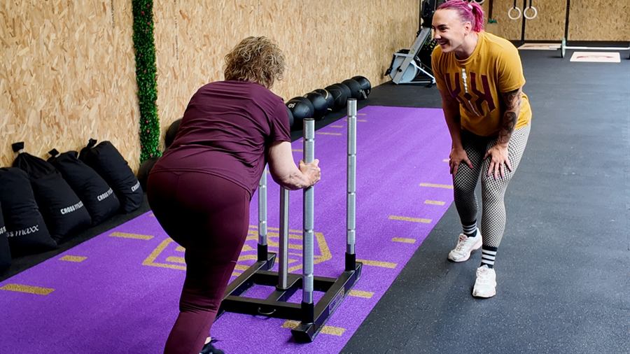 Een lid duwt de slede terwijl de coach lachend meekijkt